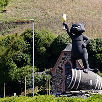 Skulptur einer schwarzen Katze, die auf einem Weinfass steht und ein Weinglas in die Höhe hält.