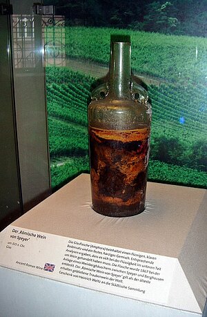 Grüne Weinflasche mit Henkeln, die mit einer bräunlichen Masse gefüllt ist