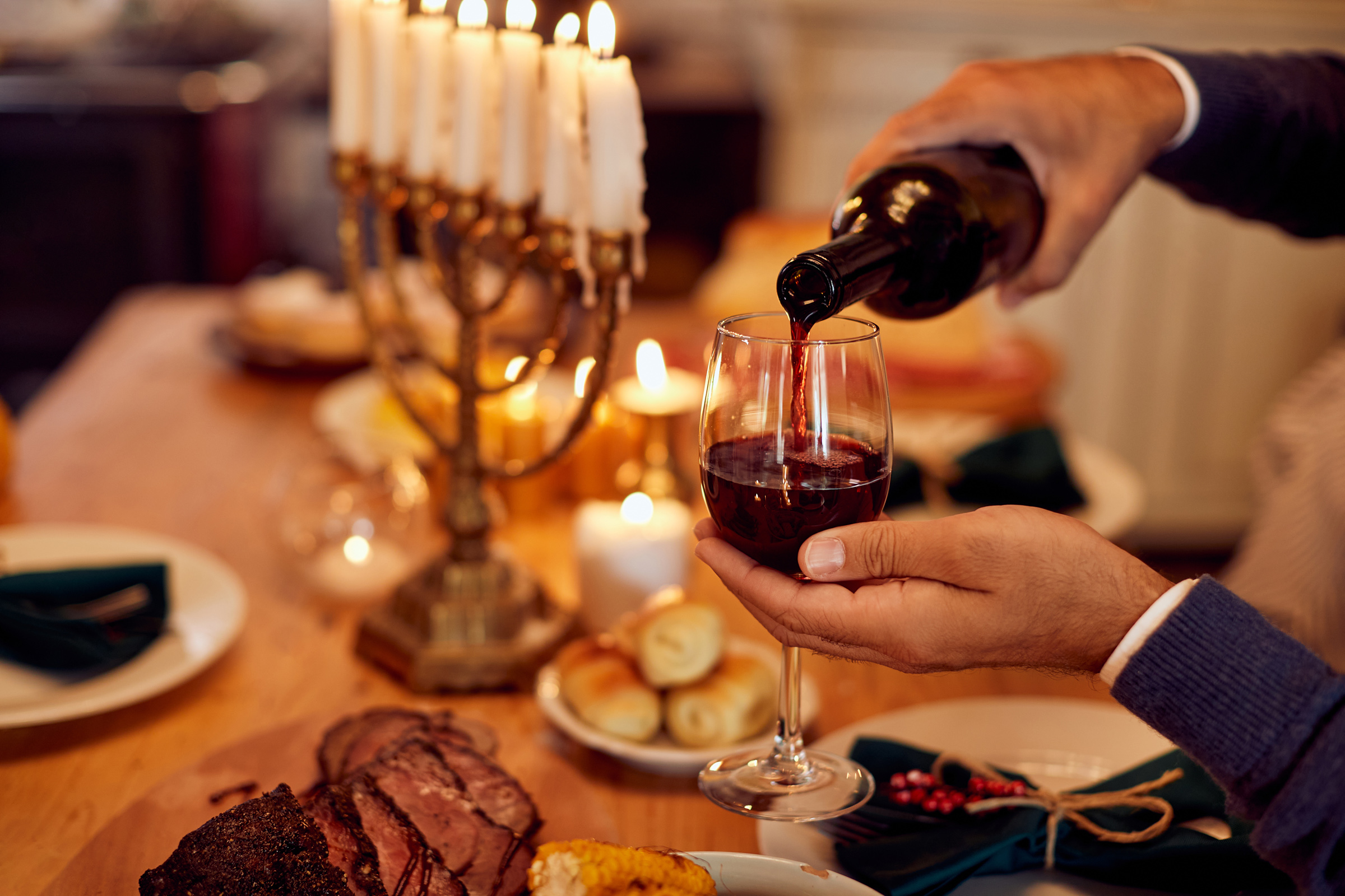 Nahaufnahme eines Mannes, der koscheren Wein in ein Weinglas gießt, während er am Esstisch Chanukka feiert.